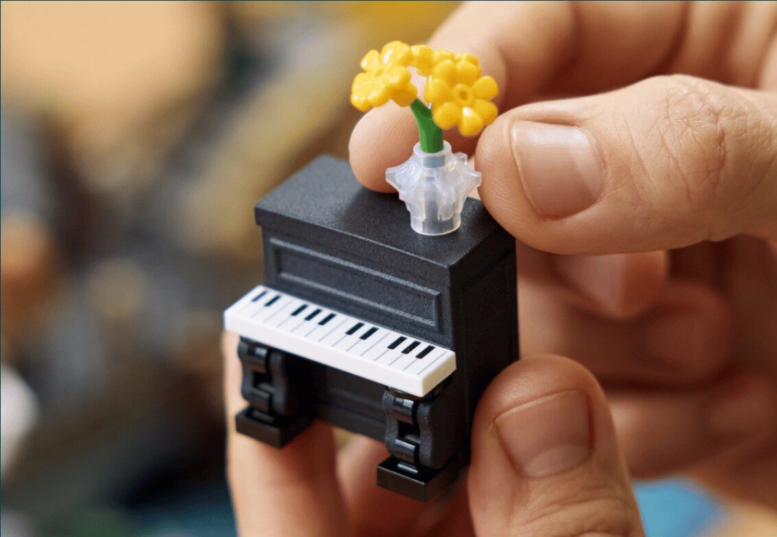 Hands holding the 3D printed LEGO street piano with a yellow flower bouquet on top